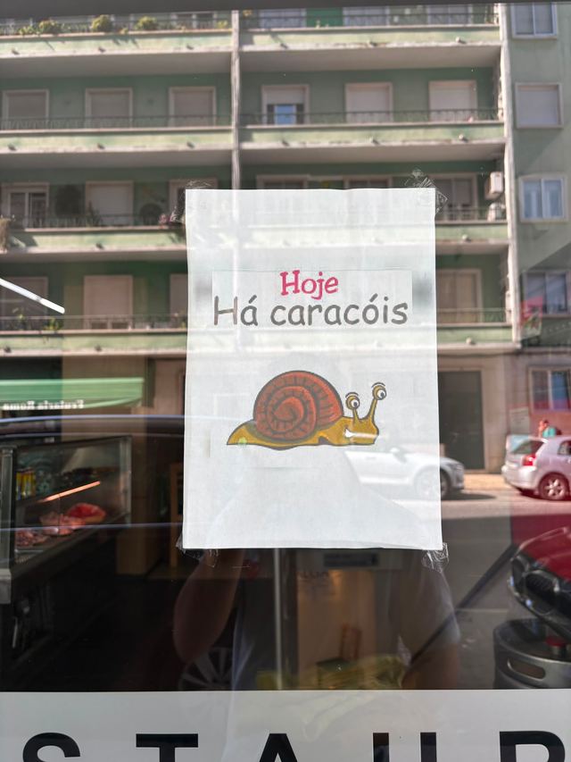 Printed sign taped to a restaurant window reading “Hoje Há caracóis”, with a cartoon snail below the words