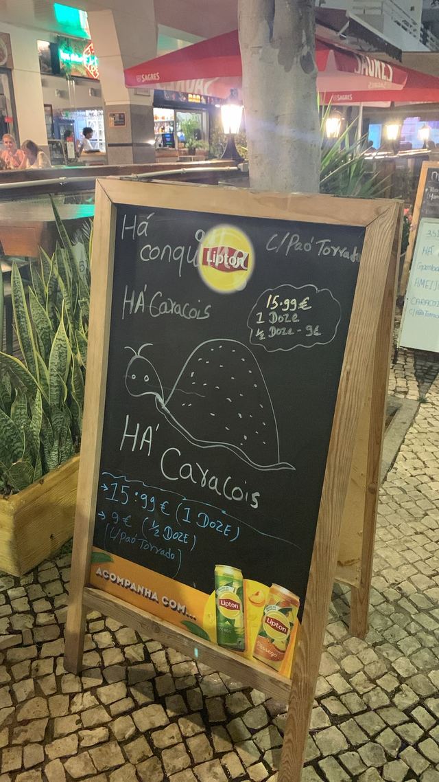 Handwritten A-board at night offering “Há Caracóis” at 15,99 euros a dozen, with a snail drawn in chalk