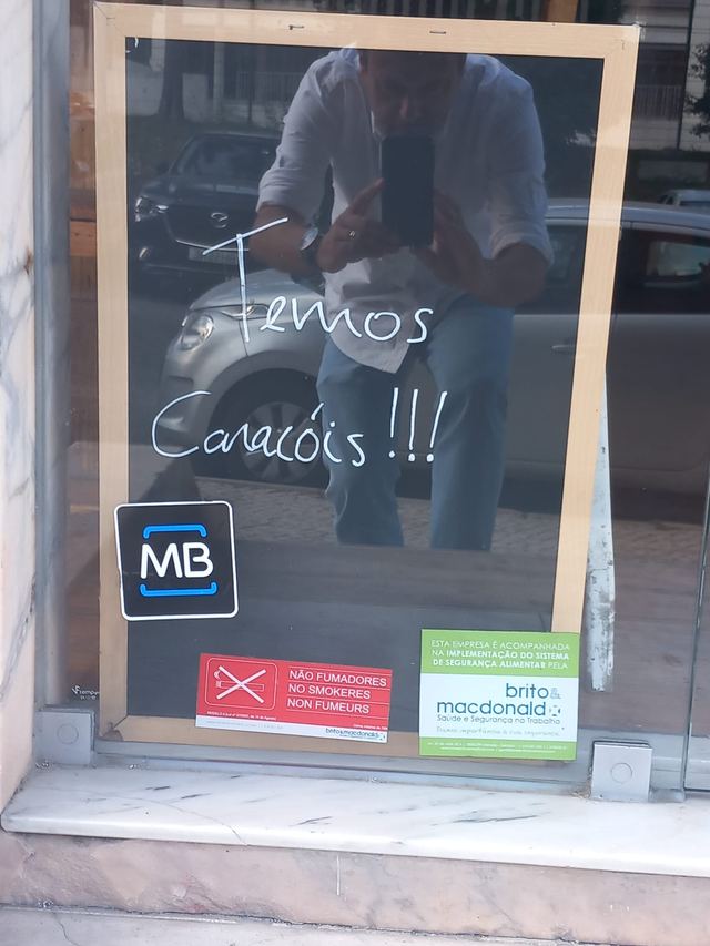 “Temos Caracóis!!!” written in white marker on a café window, above Multibanco and no-smoking stickers