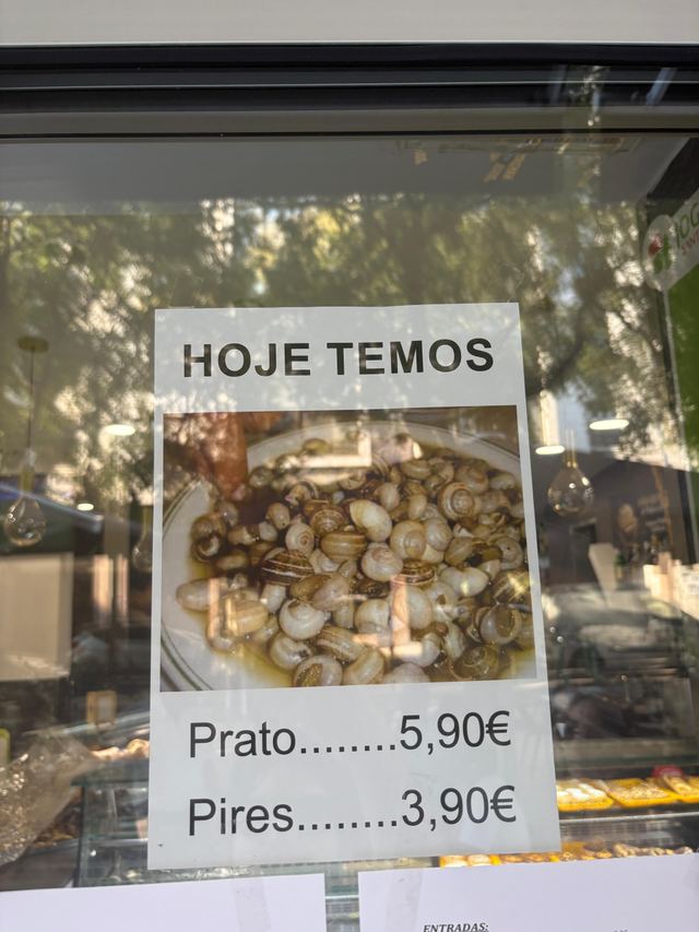 Printed window sign reading “Hoje temos” above a photo of a plate of snails, with prices for a prato and a pires